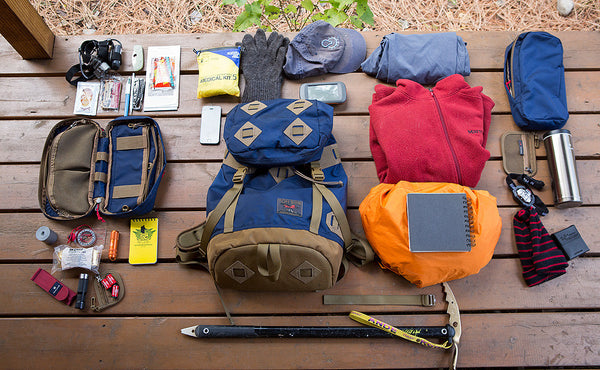 A loadout shot of the Guide's Pack with clothing, an ice axe, a pair of Side Pockets with a water bottle, a med kit, some tools and maps, and a head lamp.